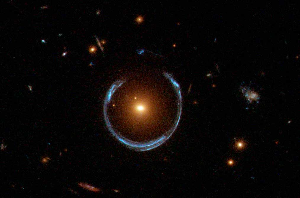 Große Massen lenken das Licht ab und wirken wie eine optische Linse und leiten das Licht einer eigentlich verdeckten Lichtquelle hinter der lichtablenkenden Masse an dieser vorbei. Die Lichtquelle erscheint dann mehrfach oder in Form eines Einsteinringes, wie hier gezeigt. Foto:  ESA/Hubble & NASA